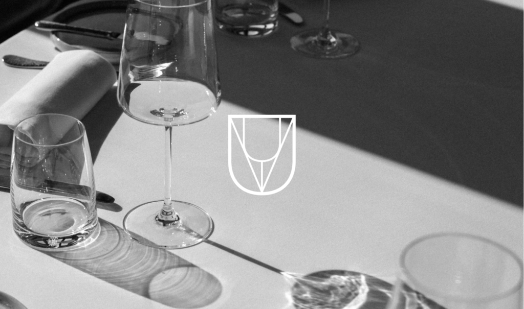 submark of vine bud logo on image of table with wine glass
